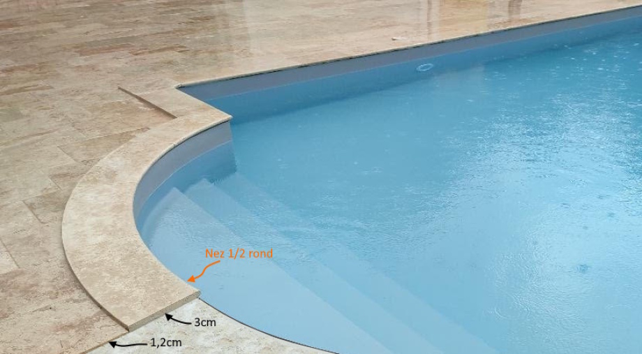 Détail de la margelle courbe en travertin beige, plage antidérapante et niveau d’eau au bord d’une piscine extérieure.